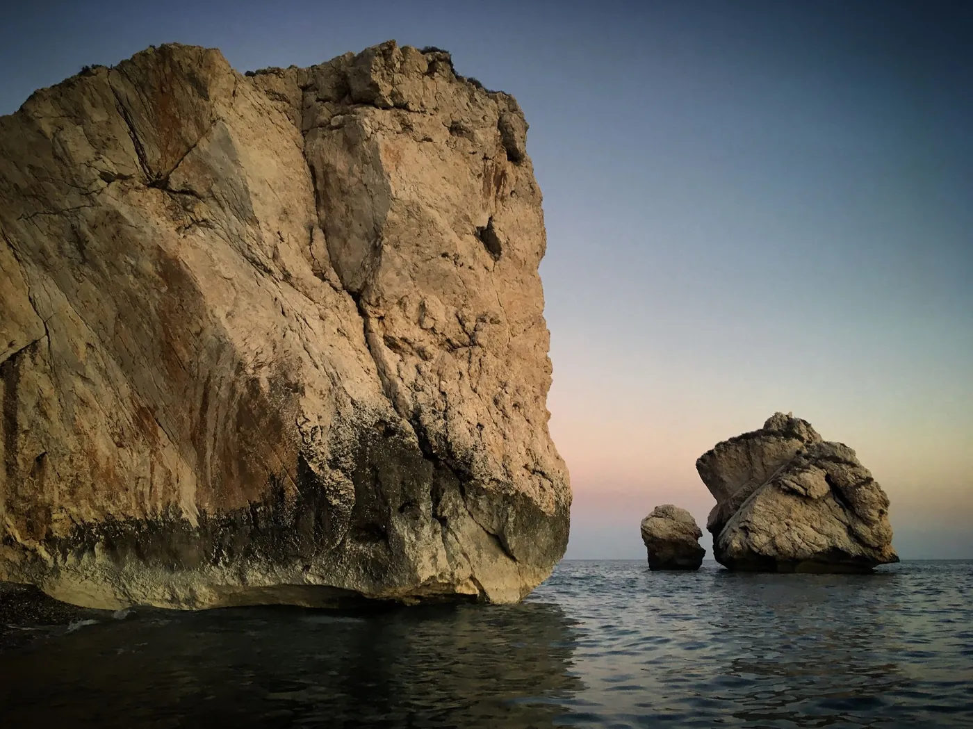 Petra tou Romiou rocks standing in a still sea at dusk near Kouklia