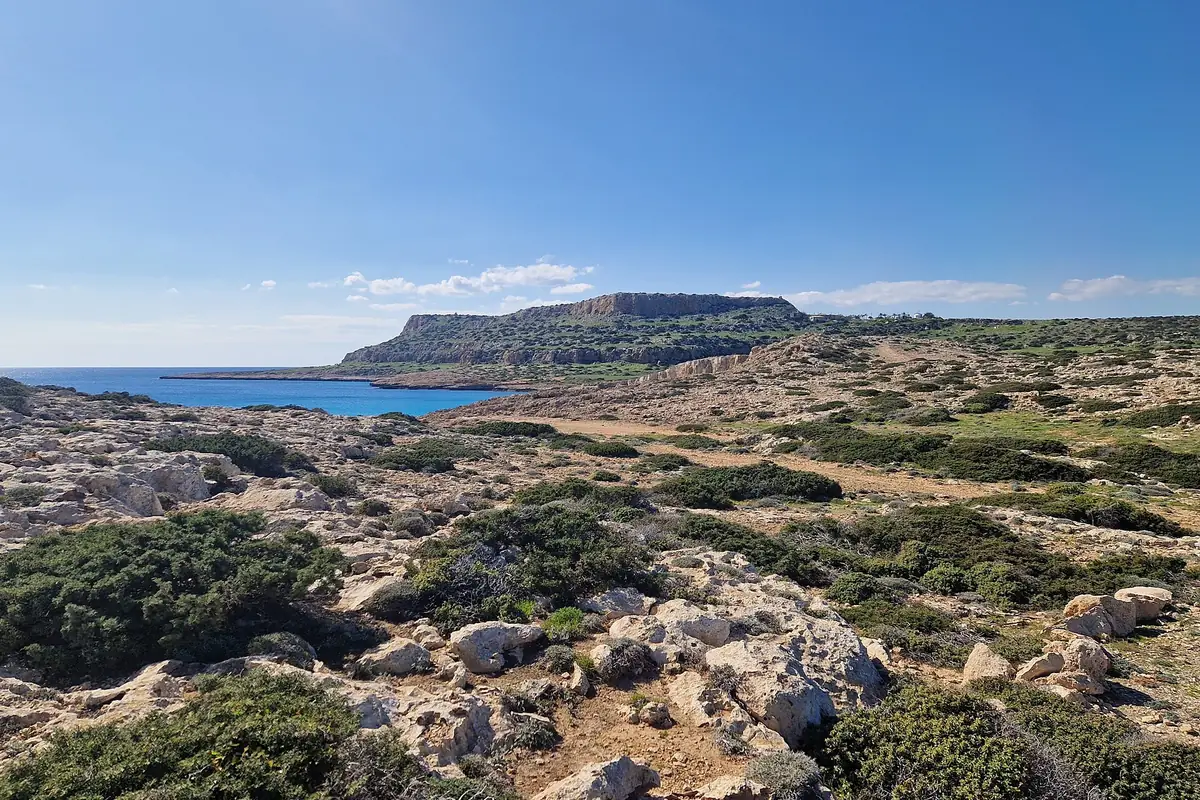 Rocky scrubland on the Cape Greco plateau with the flat-topped headland and a blue bay behind